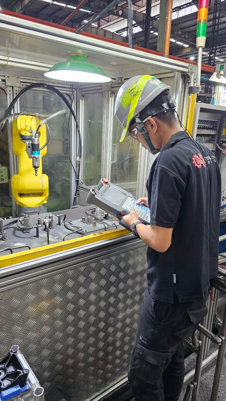 Sapotoya engineer using a teach pendant to program a robot inside a fenced automation cell