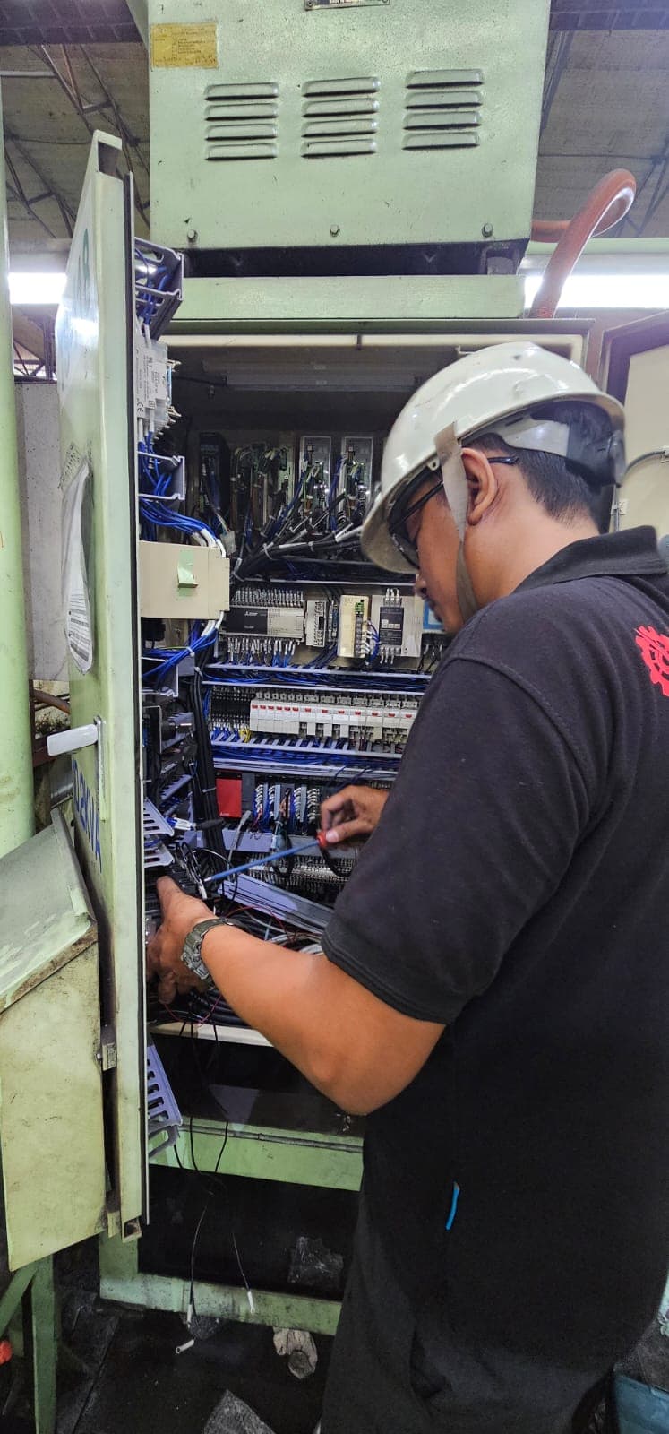 Sapotoya technician working inside an open machine control cabinet, wiring terminals and PLC modules
