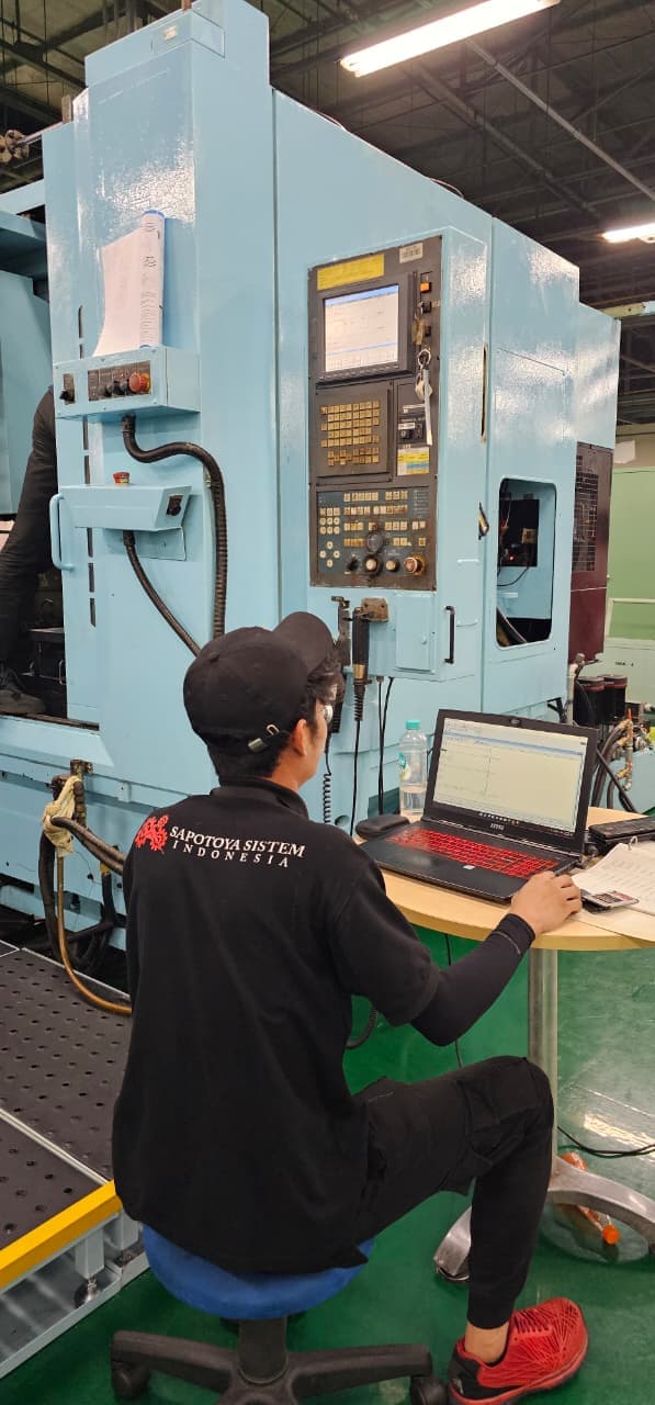 Sapotoya engineer at a laptop beside a CNC machining centre, working on the machine control program