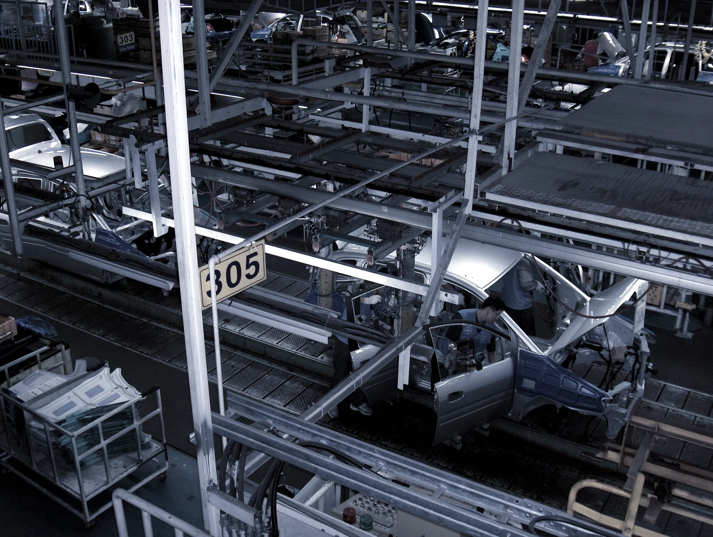 Vehicle bodies moving along an automotive assembly line with overhead conveyor structures
