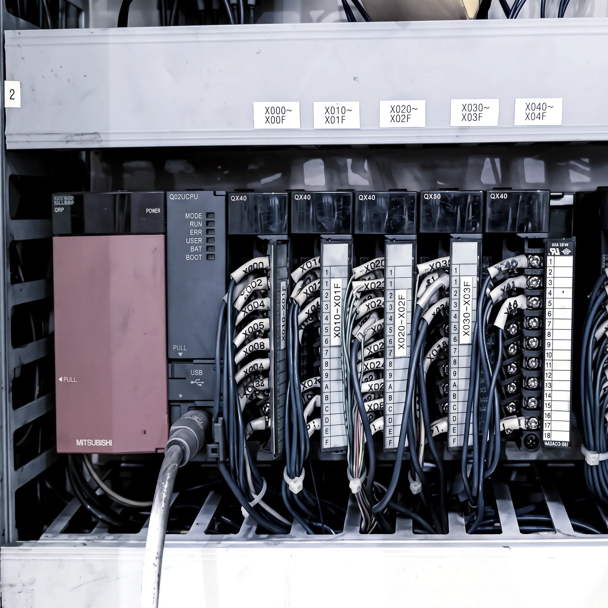 Mitsubishi PLC rack inside a machine control cabinet, its input modules labelled by address range and wired to numbered field terminals