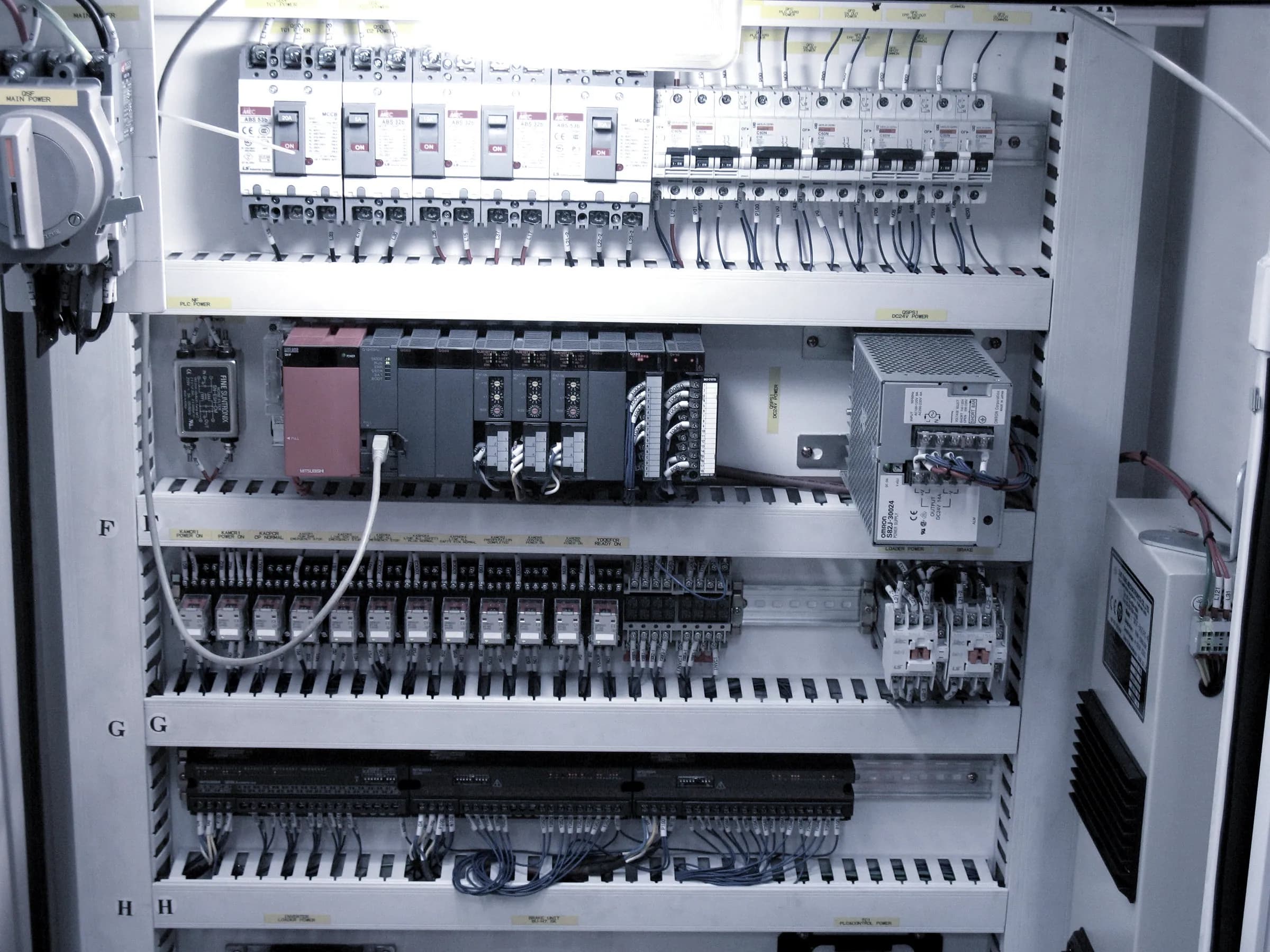 Interior of an industrial control cabinet showing circuit breakers, PLC modules and relay terminals