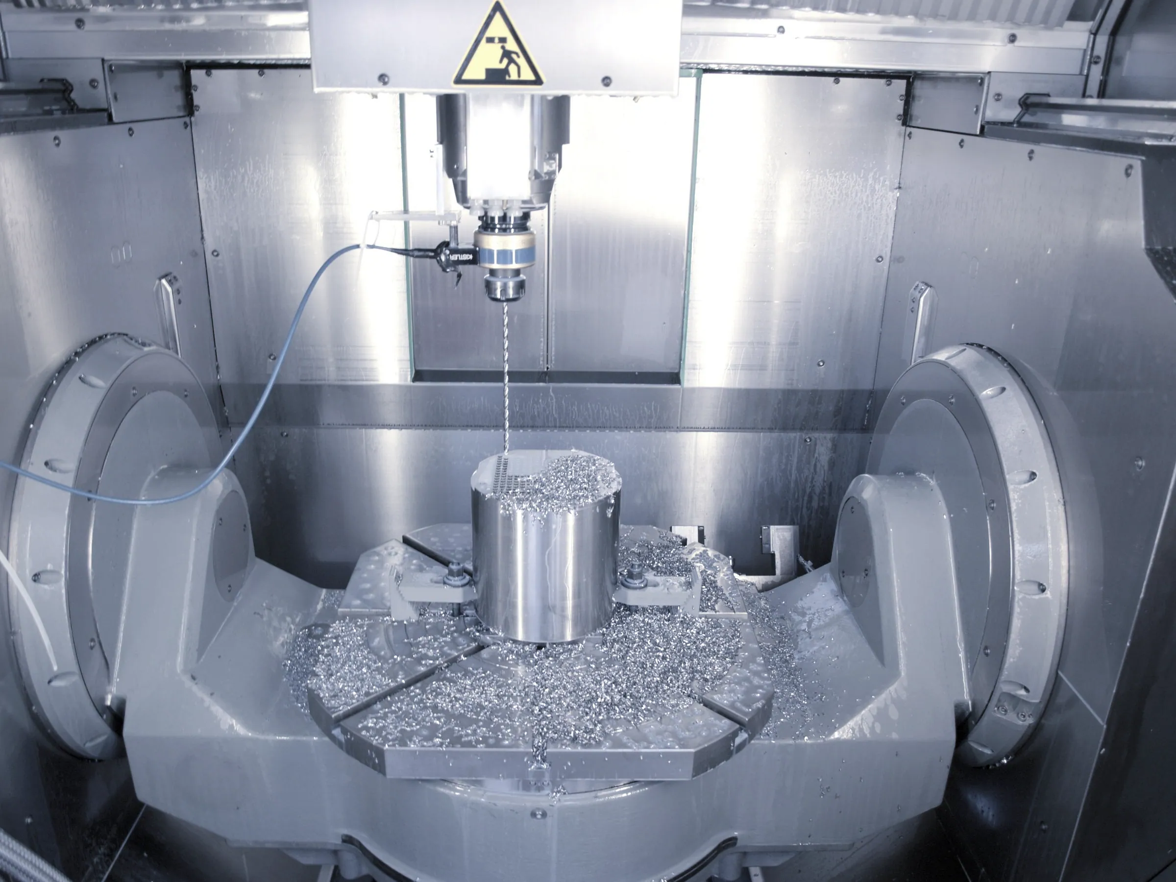 Close-up inside a machining centre as the spindle drills a steel component surrounded by metal chips